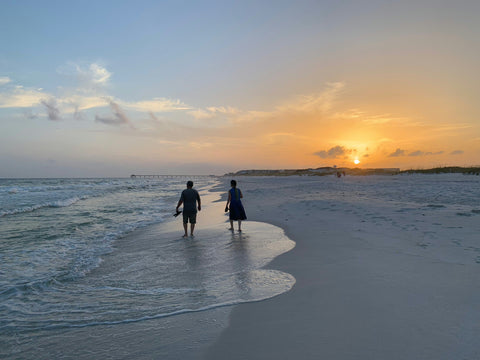 Two silhouetted figures walking on the shoreline at sunset for stunning beach photos.